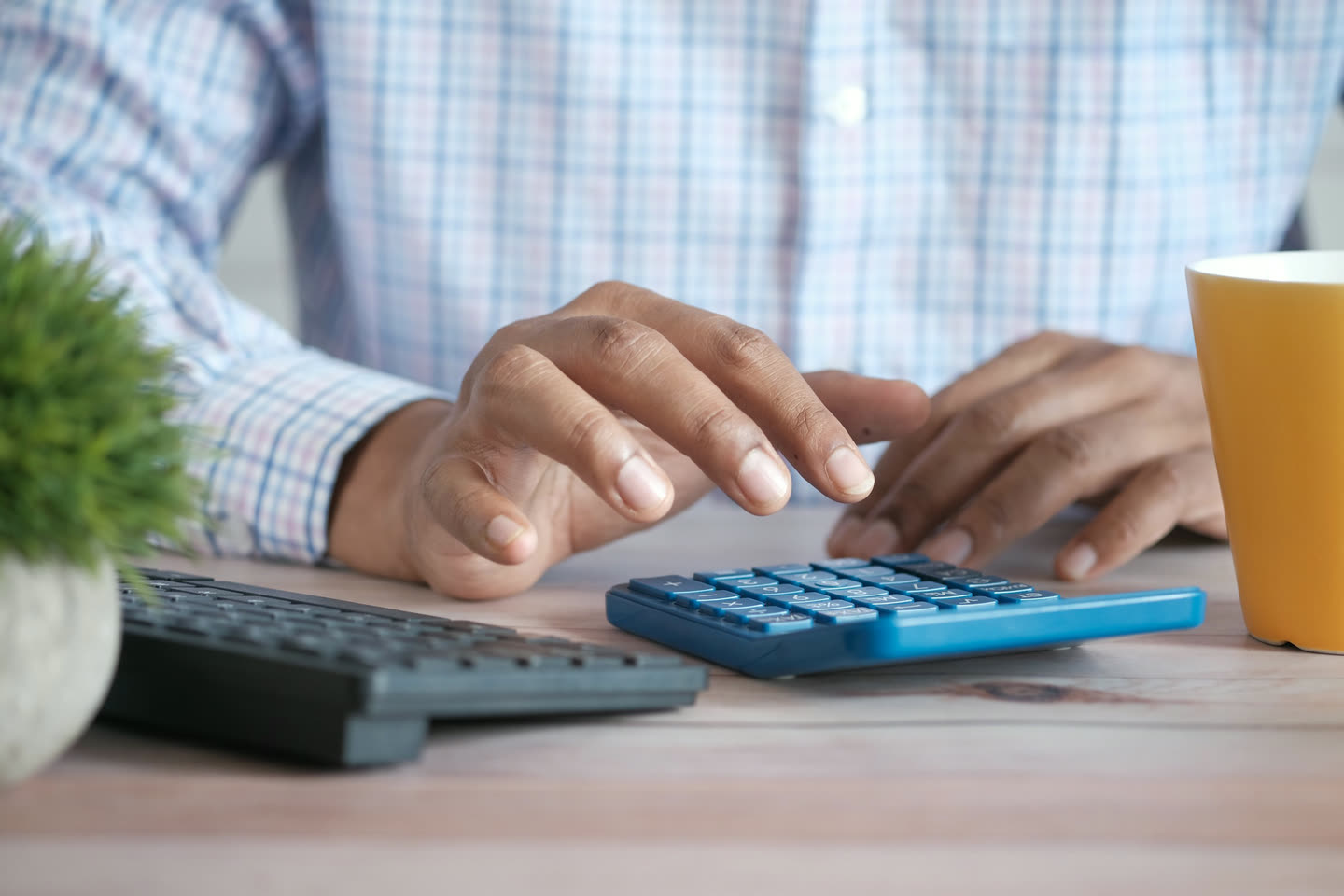 Mãos fazendo contas em uma calculadora azul sobre a mesa de trabalho