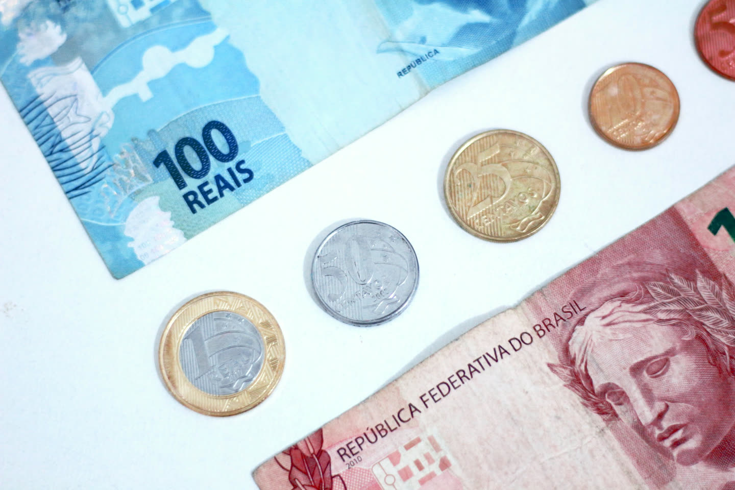 Cédulas de 100 e de 10 reais com moedas sobre uma mesa branca