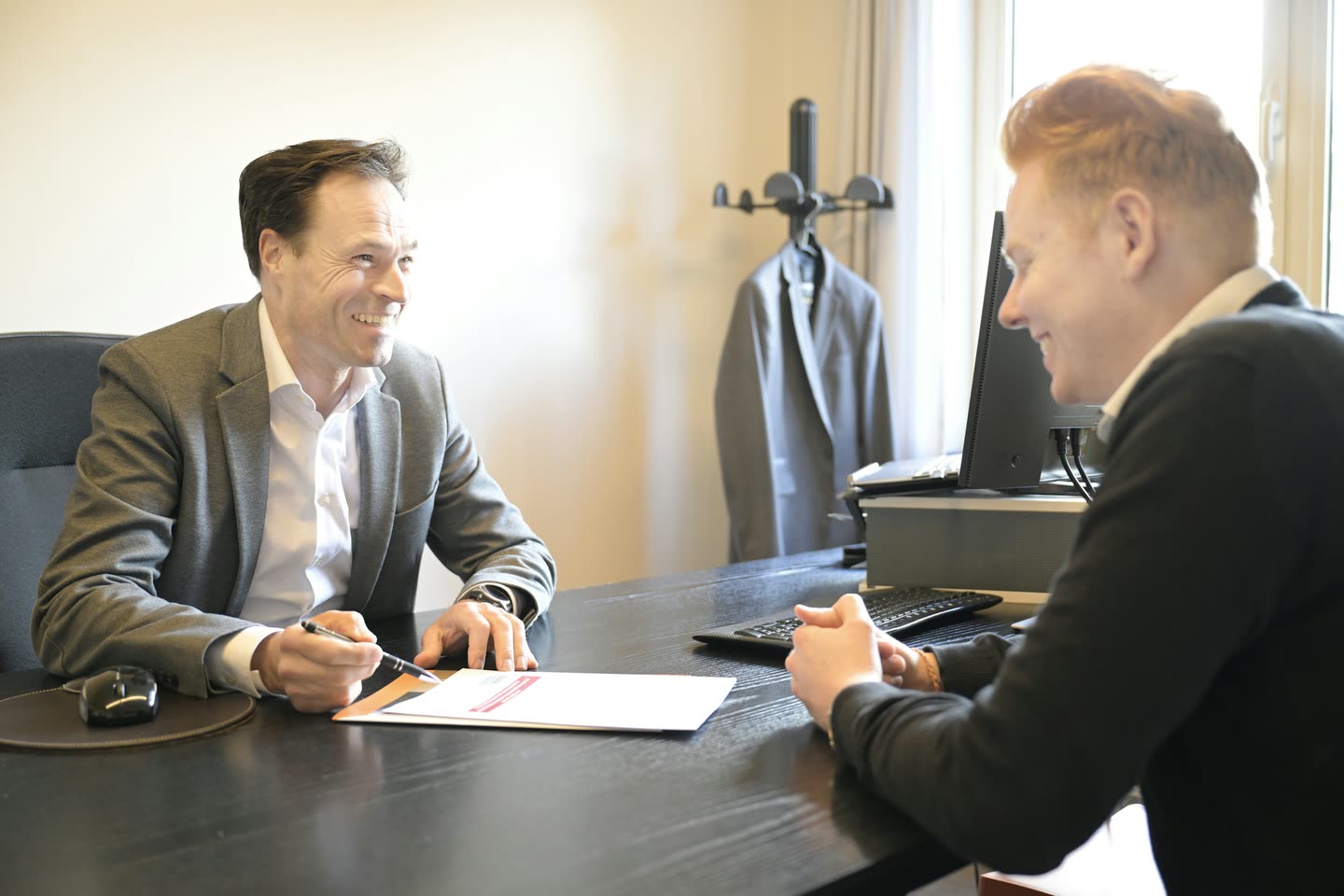 Profissional sorrindo enquanto preenche um documento com um cliente à mesa