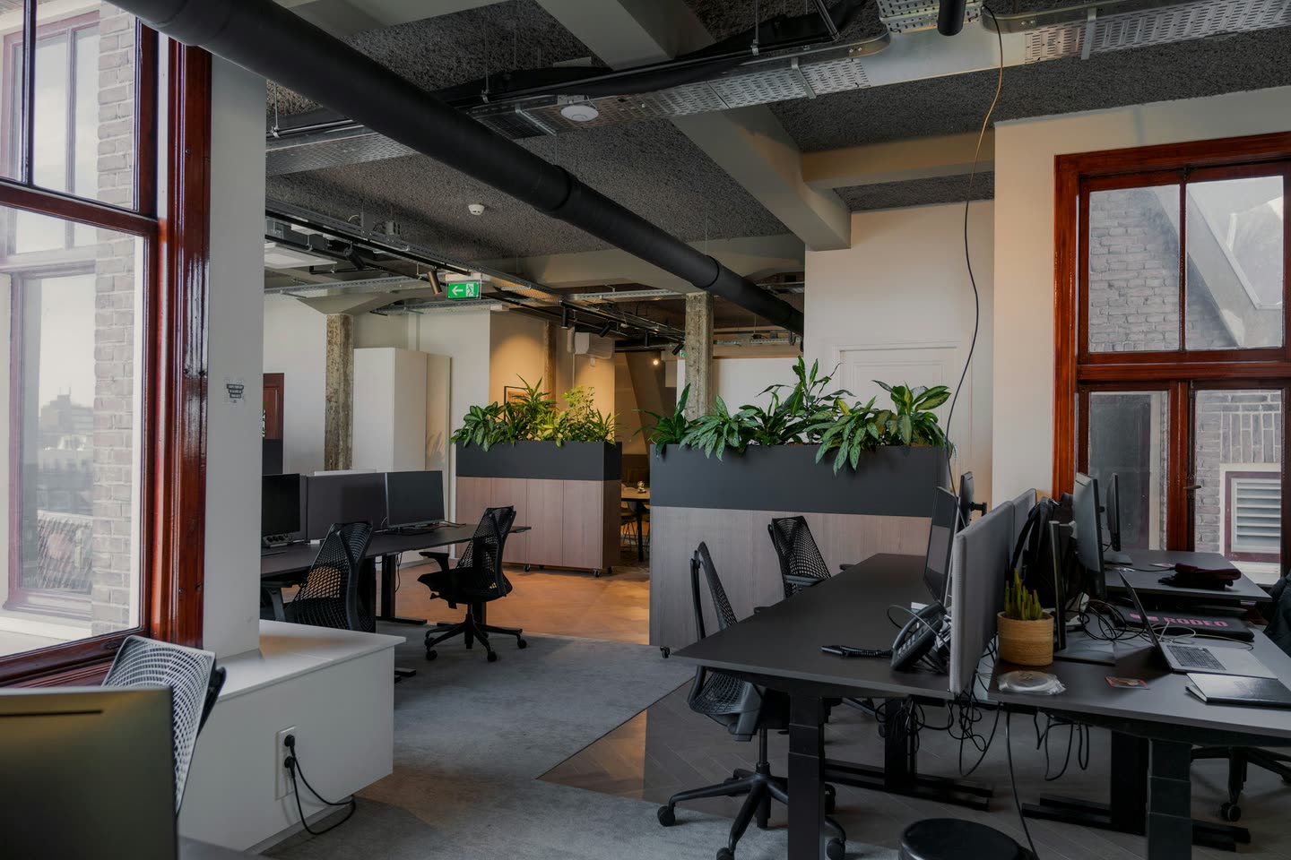 Escritório com mesas de trabalho, computadores e floreiras de plantas